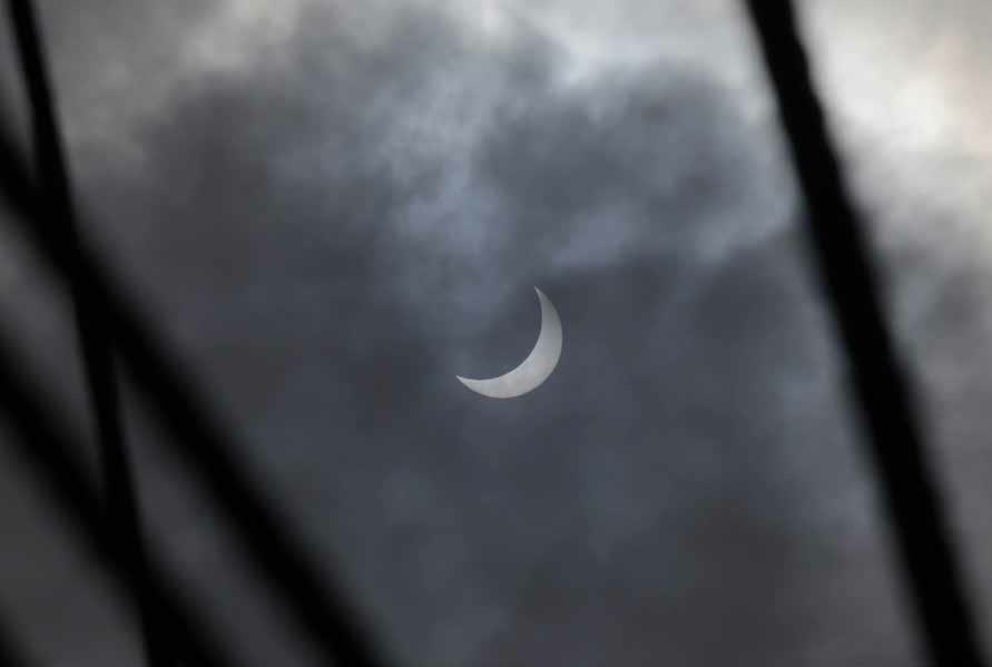 Sichelförmig verdeckte Sonne hinter dünnen Wolken, davor Takelage