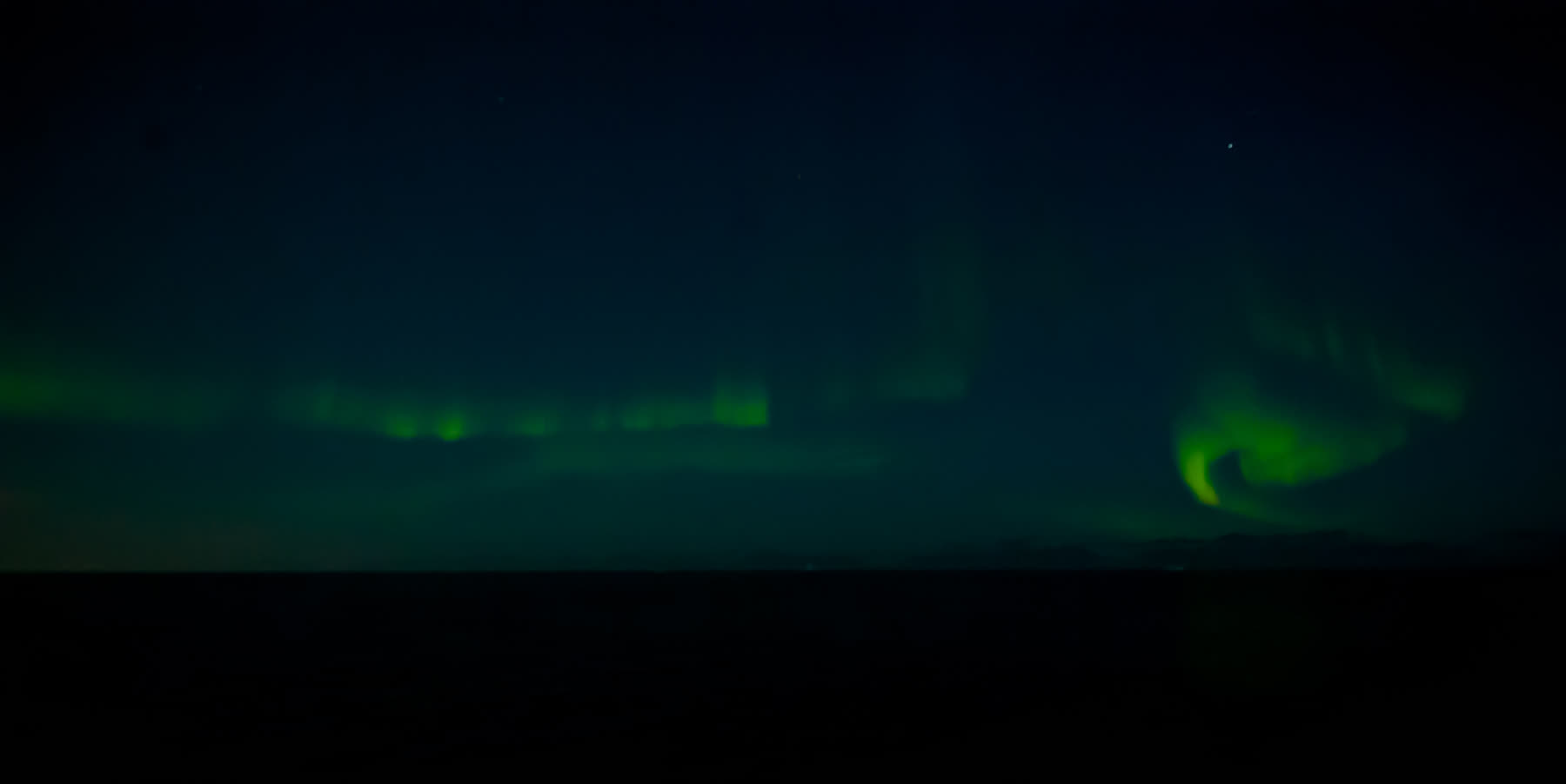 Nordlicht über dem dunklen Horizont in Nordostgrönland