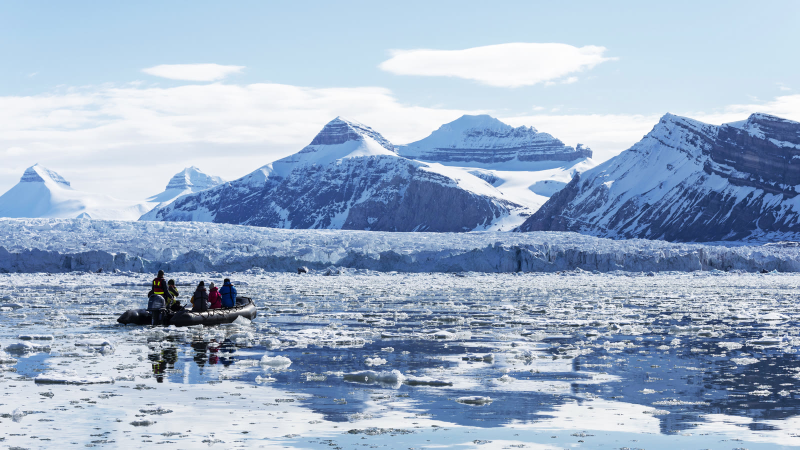 Zodiac vor einer mächtigen Gletscherfront auf Spitzbergen, ringsum treibt Eis im tiefblauen Wasser