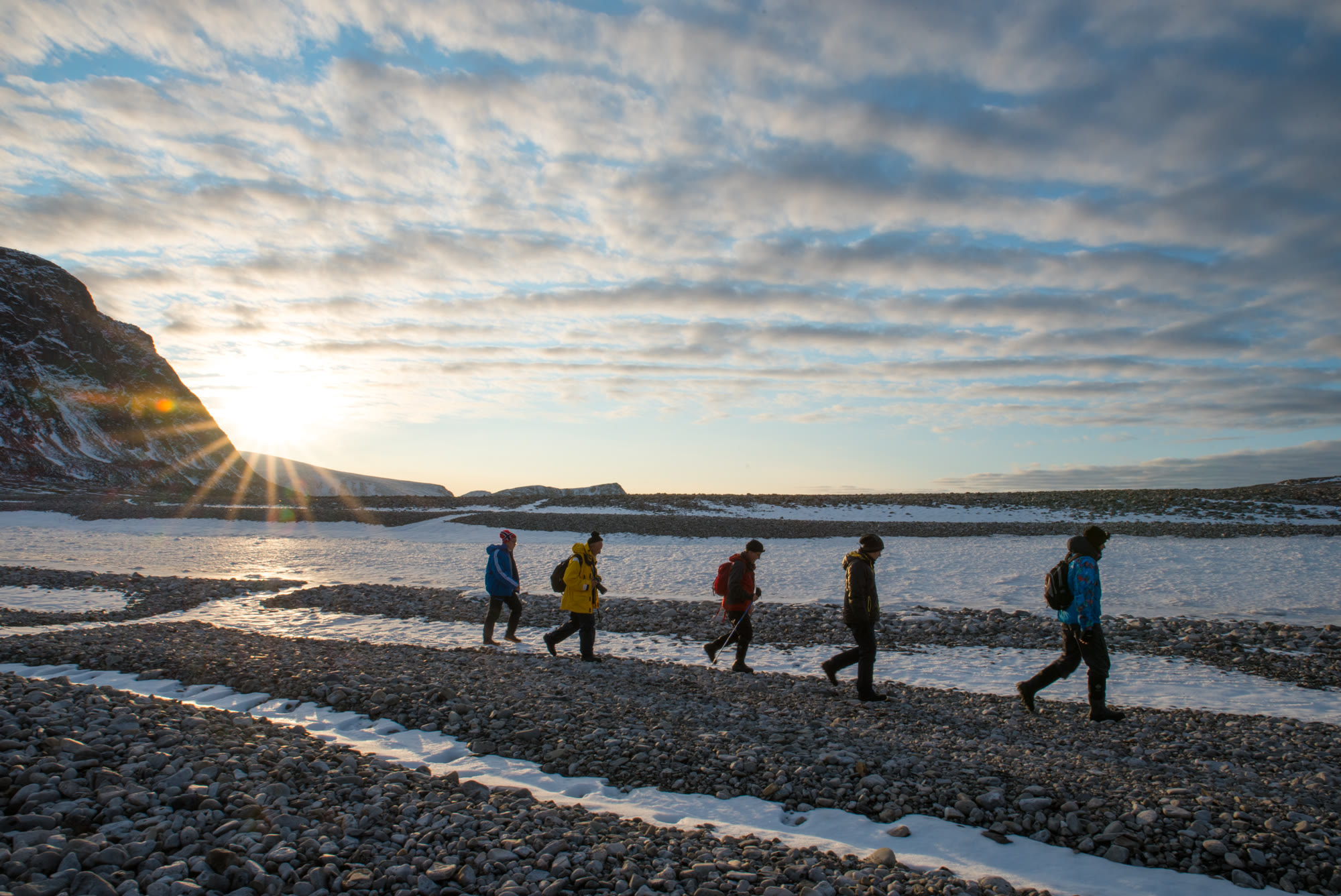 Kleine Wandergruppe auf einem Kiesstrand auf Spitzbergen im Gegenlicht der tiefstehenden Sonne