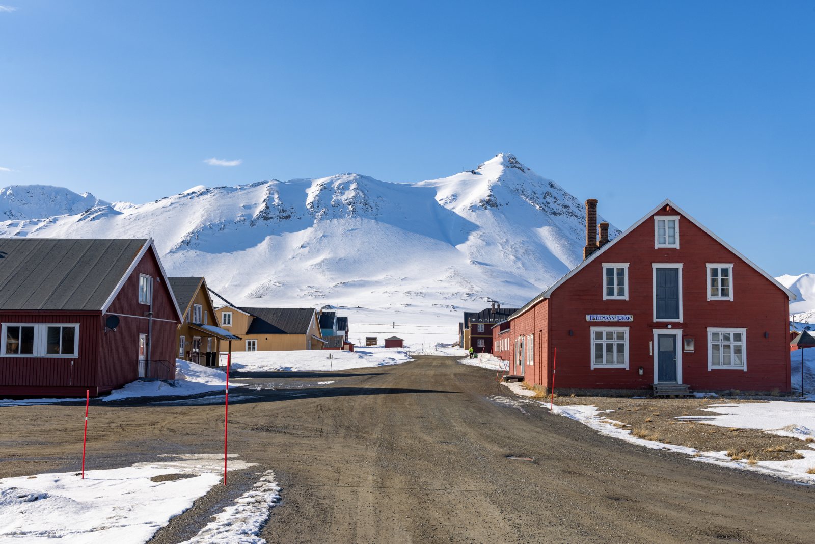 Rote Holzhäuser der Forschungssiedlung Ny-Ålesund vor schneebedeckten Bergen