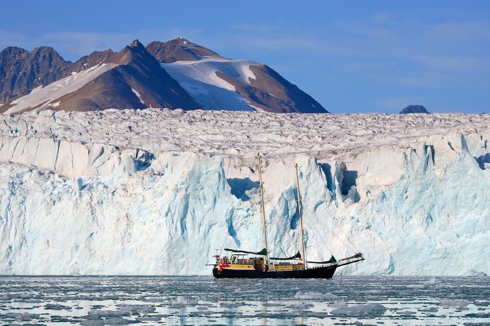 Die Meander vor einer breiten, hellblauen Gletscherfront in Spitzbergen