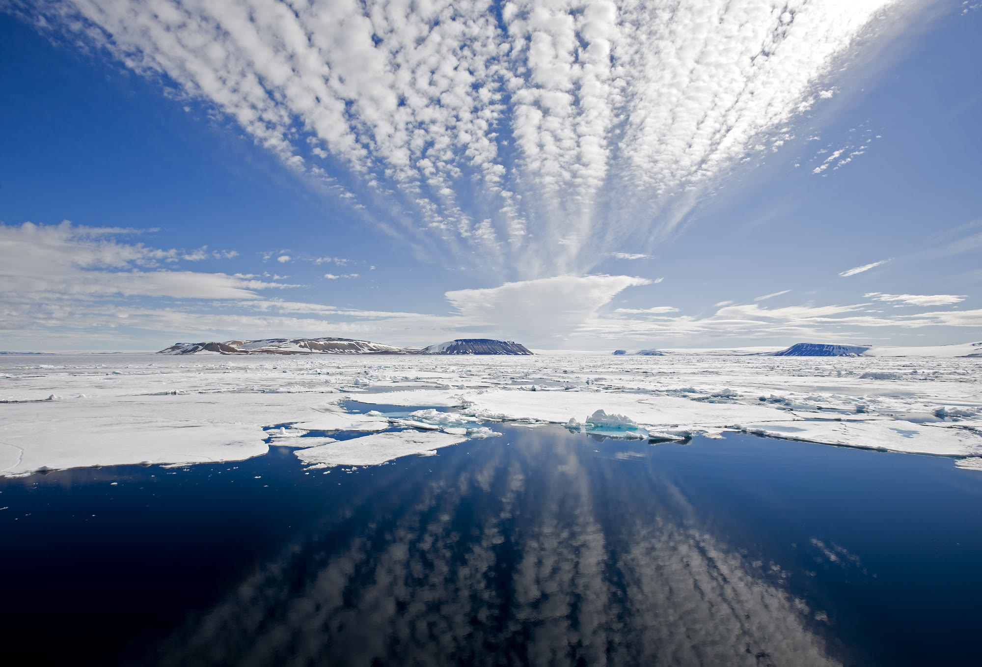 Packeis nördlich von Spitzbergen im Juli, offene Wasserflächen zwischen Eisschollen unter blauem Himmel