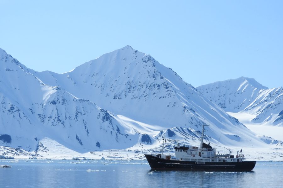 Kleines Expeditionsschiff vor verschneiten Bergen in einem Fjord Spitzbergens
